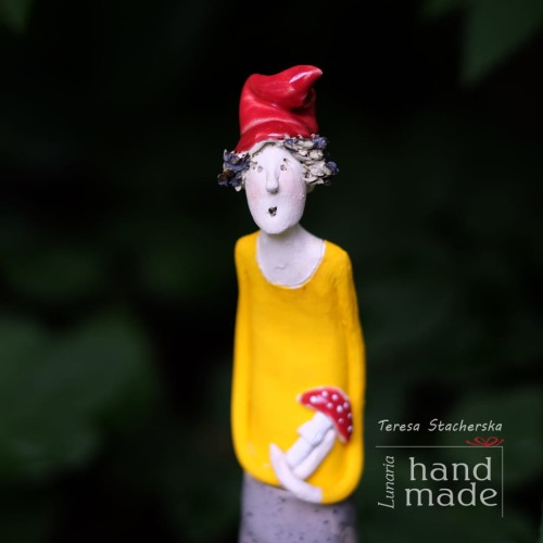 Ceramiczna stojąca figurka uśmiechniętego skrzata w żółtej bluzie i czerwonej czapce trzymającego muchomora w ręku.jpg